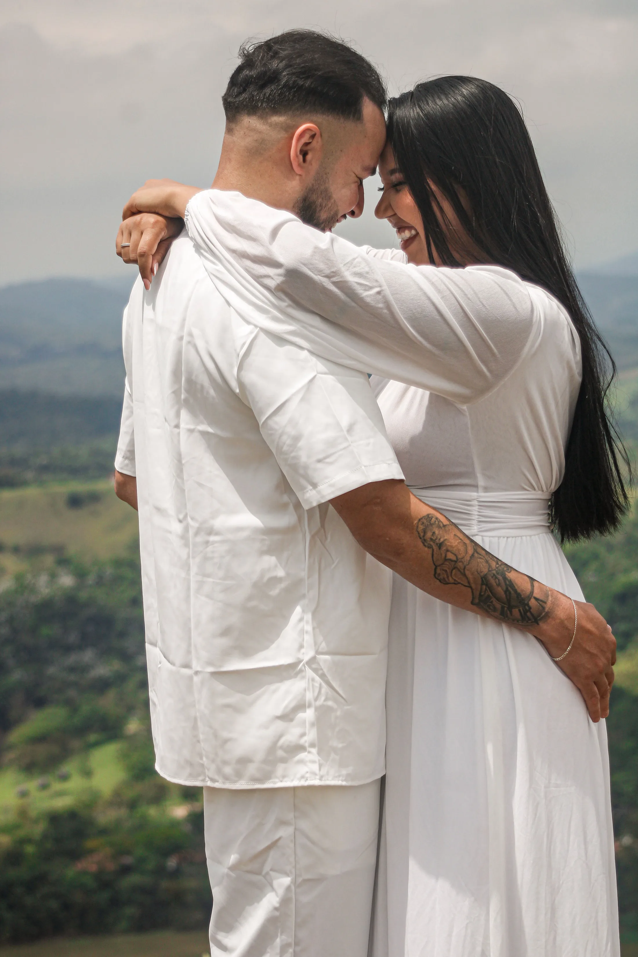 Casal abraçado com as testas encostadas, com montanhas ao fundo.