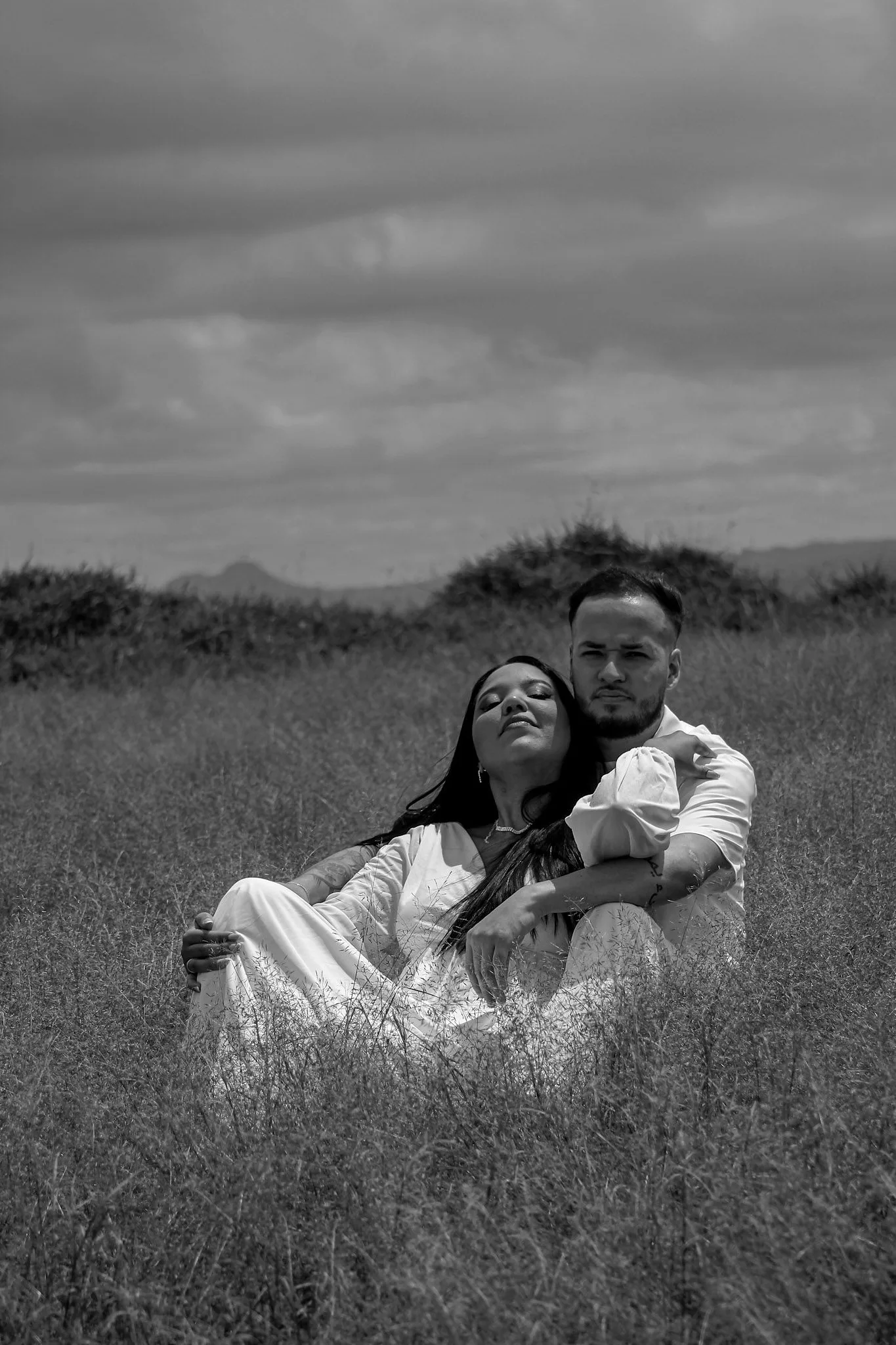 Casal sentado em um campo de grama, em preto e branco.