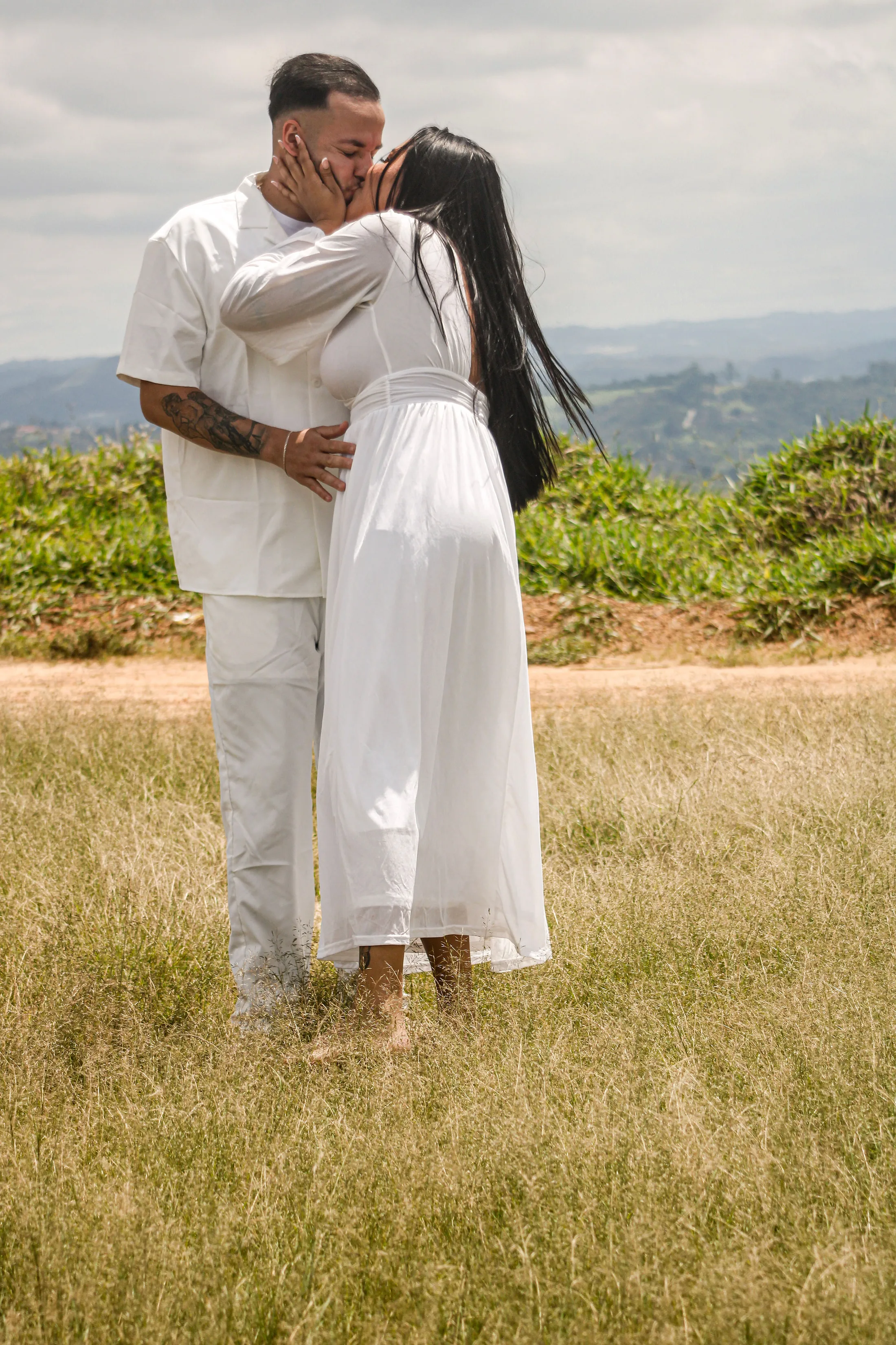 Casal se beijando em um campo de grama, em plano aberto.