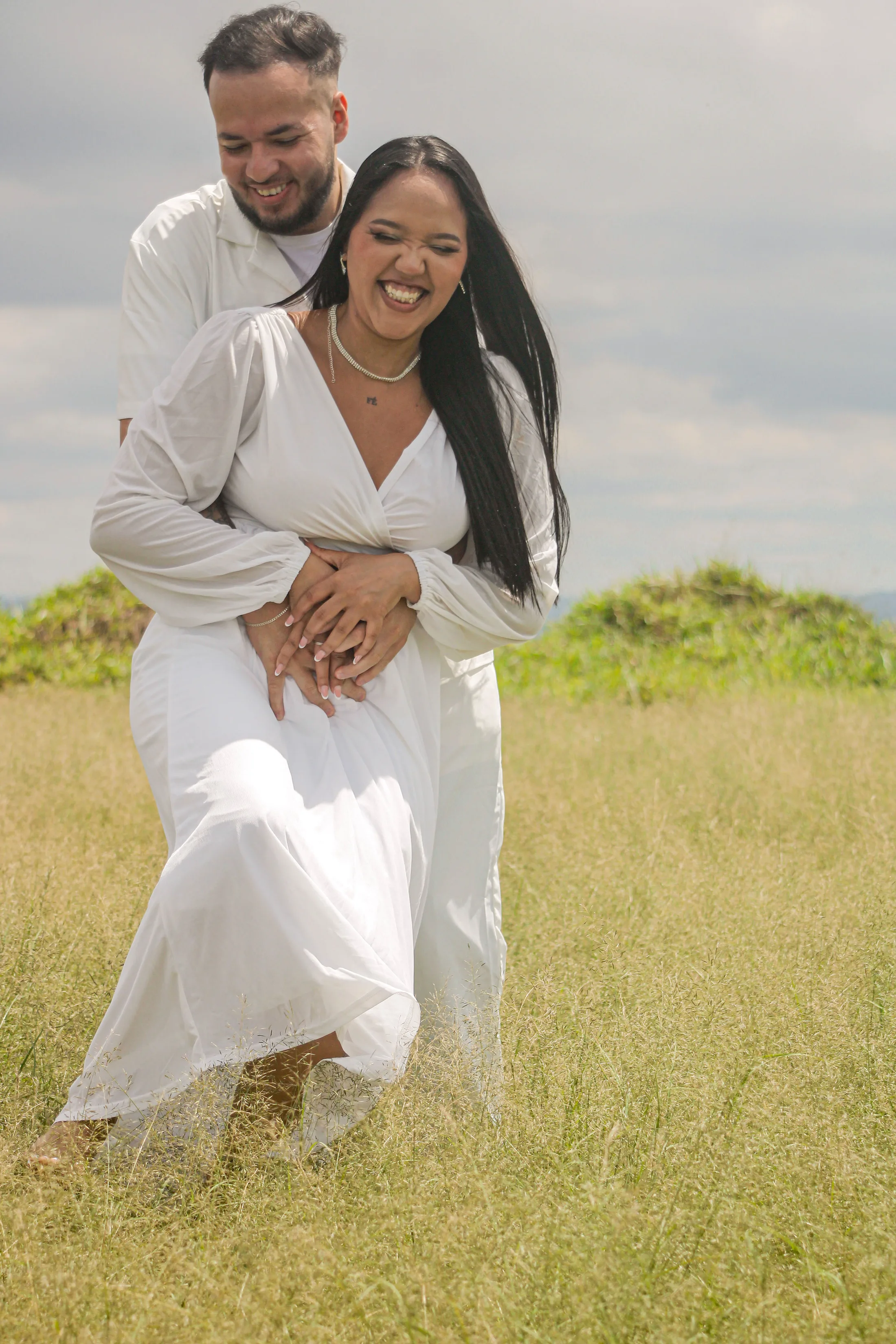 Casal sorrindo e se abraçando em um campo de grama.