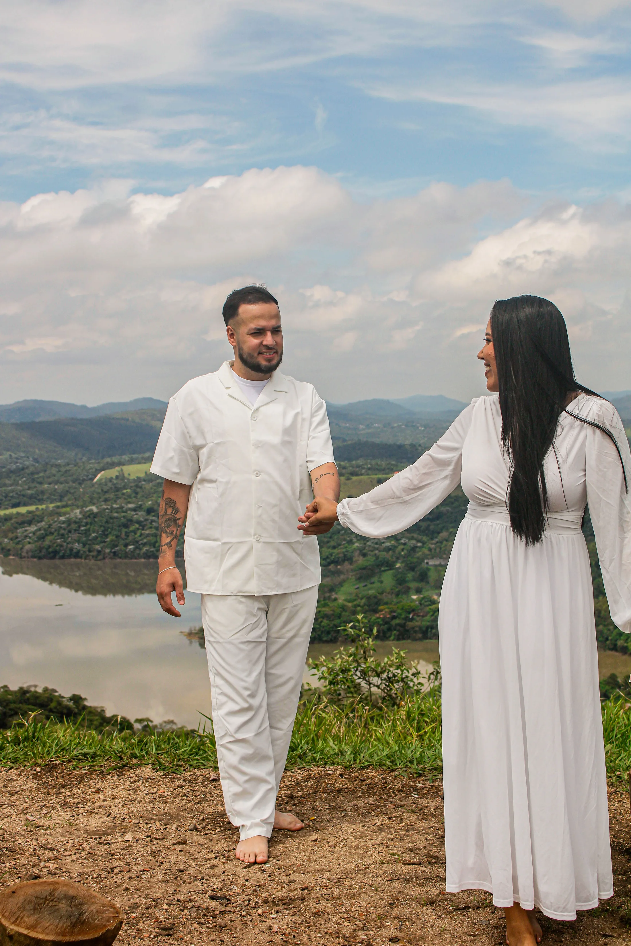 Casal de roupas brancas de mãos dadas, de pé em um mirante.