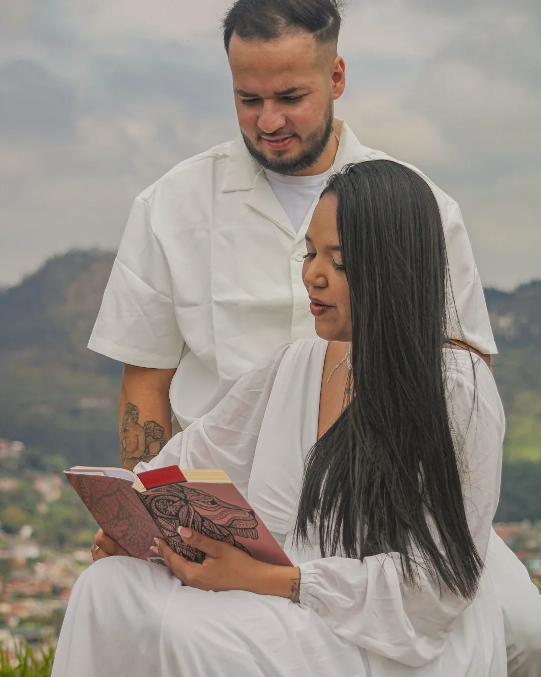 Casal sentado em um mirante, olhando para um livro aberto.
