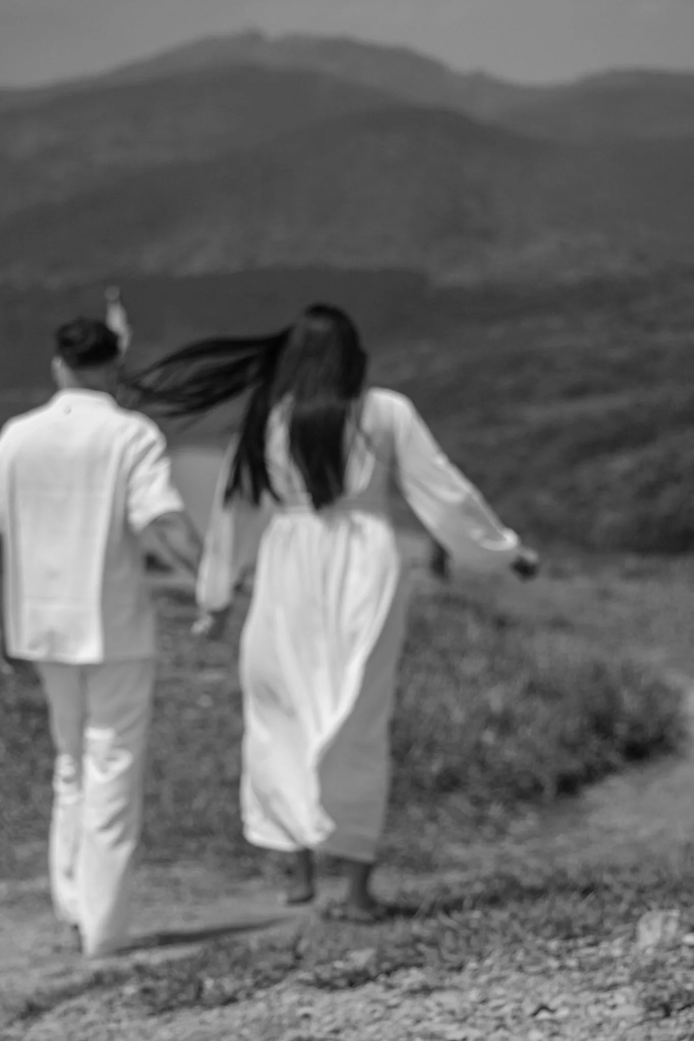 Casal caminhando de costas por uma trilha, em preto e branco.